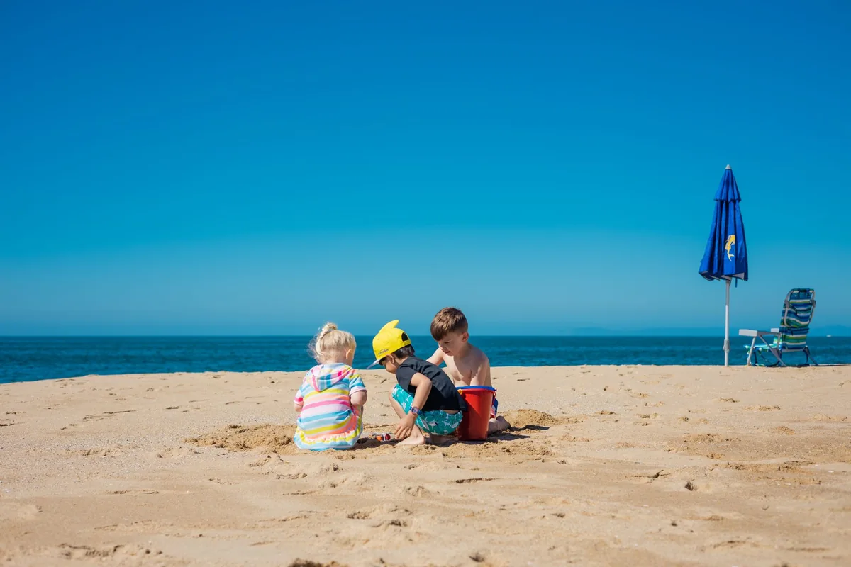 Drei Kinder spielen gemeinsam an einem Sandstrand